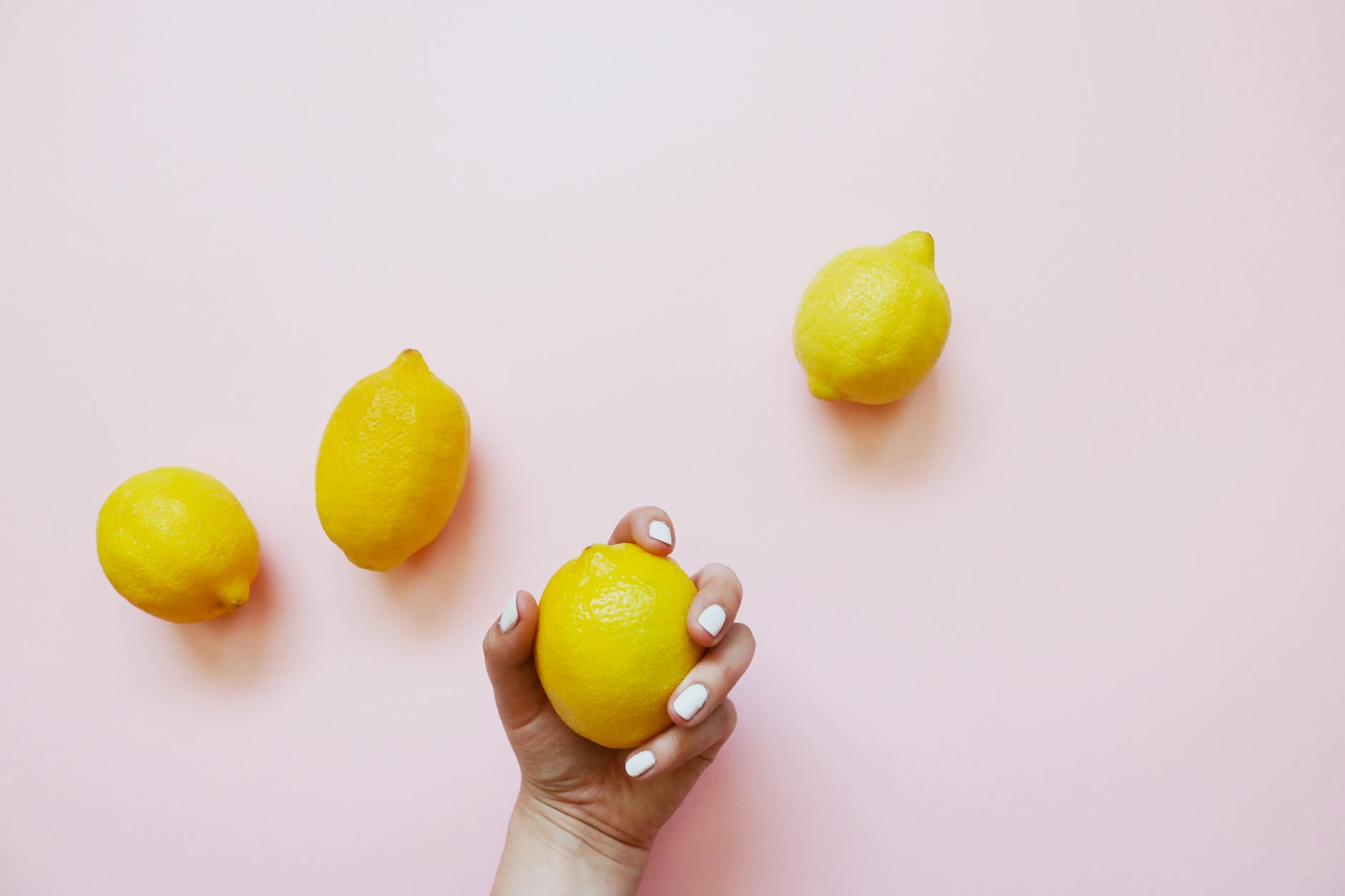 A hand holding a fresh lemon on soft pink background, representing natural approaches to clitoral health.