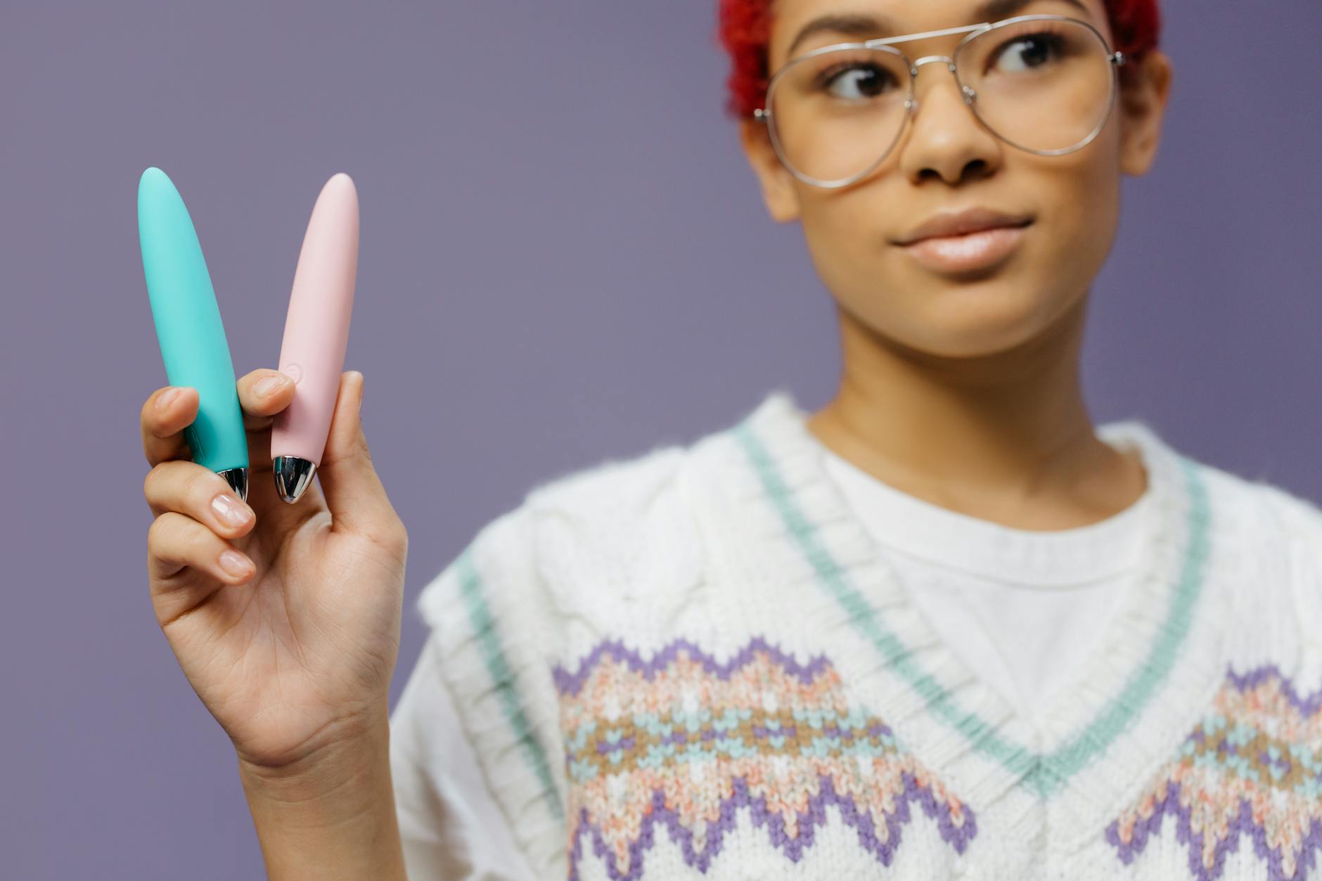 Junge Frau mit bunten Vibratormodellen vor violettem Hintergrund, die verschiedene Optionen für Anfängerinnen zeigt