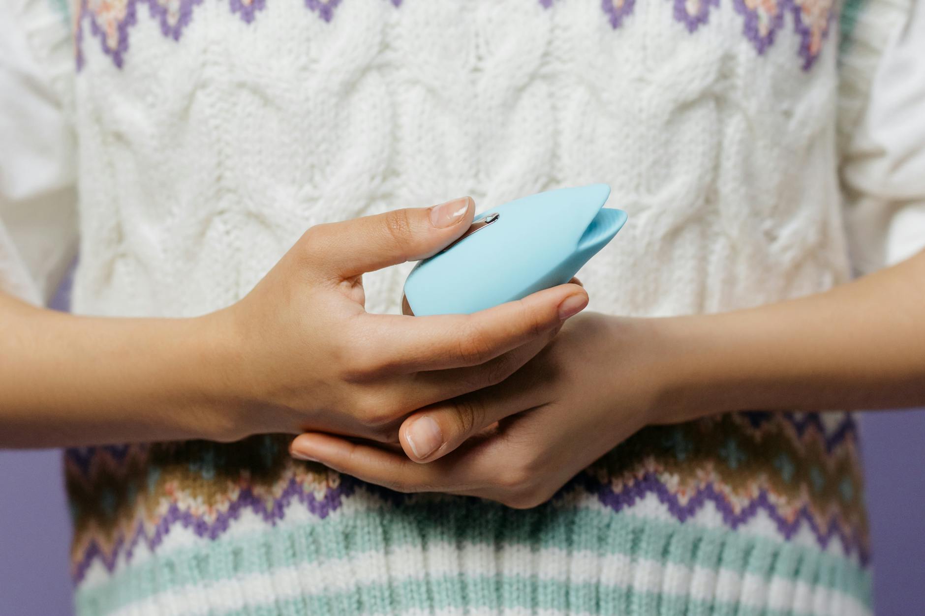 Nahaufnahme von Händen, die einen blauen persönlichen Massager gegen einen gestrickten Pullover halten.