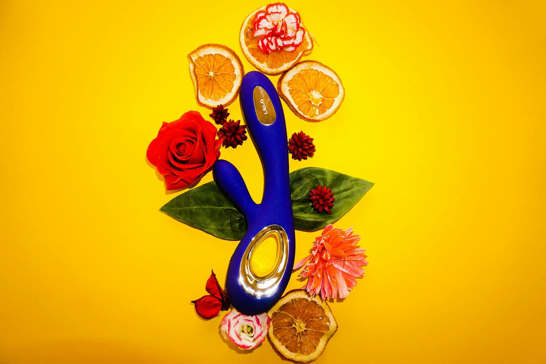 Eine Hand hält einen orangefarbenen Vibrator gegen einen minimalistischen lila Hintergrund